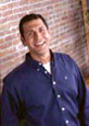 Professional man in blue shirt smiling against brick wall for orthodontics practice.