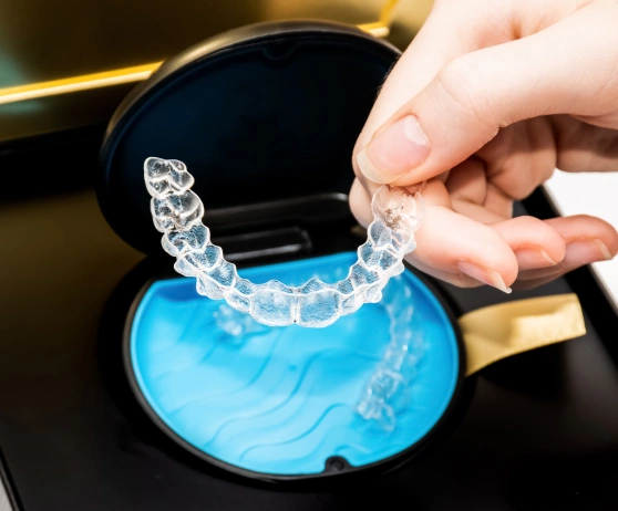 Person holding clear orthodontic aligner above blue storage case with dental tray inside.