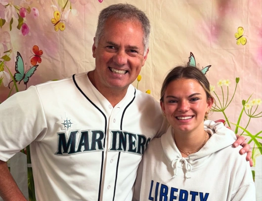 Two people smiling together wearing baseball and sports apparel against floral background.