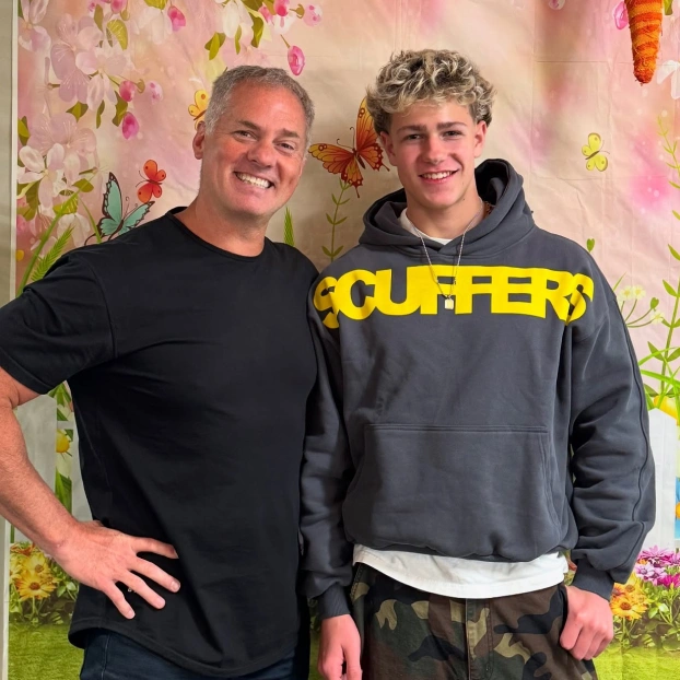 Two people smiling at camera in front of colorful floral backdrop at orthodontics office.
