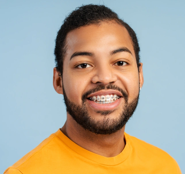 Smiling man in yellow shirt against blue background, orthodontics patient portrait