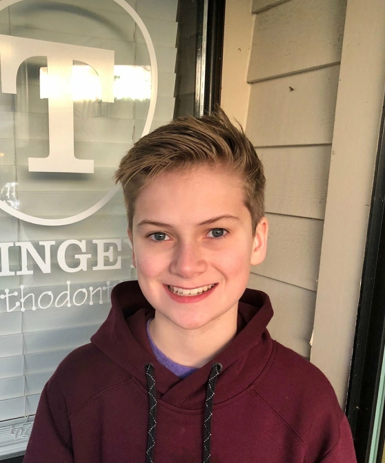 Young person smiling at camera in orthodontics office lobby wearing maroon hoodie.