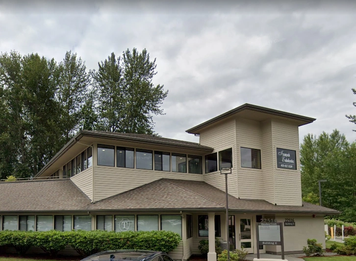 Modern two-story orthodontic office building with tan exterior and large windows surrounded by trees.