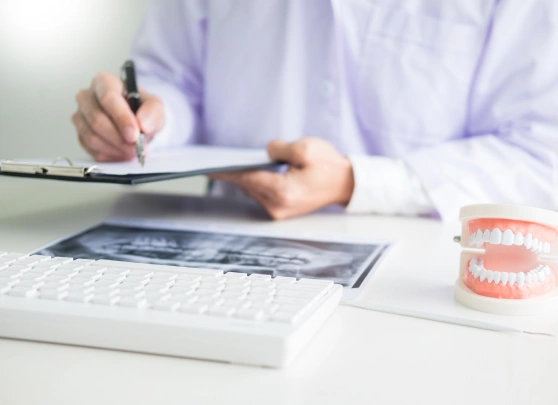 Orthodontist reviewing dental X-rays at desk with teeth model and clipboard