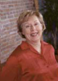 Woman in red shirt smiling at camera against brick wall background.