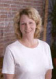 Professional headshot of woman with blonde hair against brick wall background for orthodontics practice.