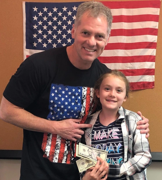 Adult and child posing together with American flag backdrop in orthodontic office setting.