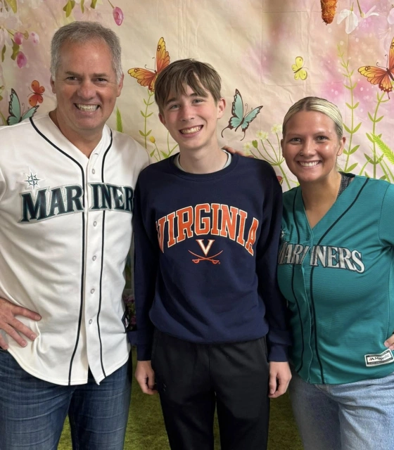 Three people smiling together wearing sports team apparel in front of floral backdrop.