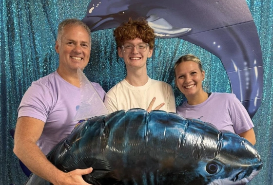 Three people holding large fish in front of blue backdrop at orthodontics event.