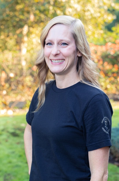 Woman smiling outdoors wearing dark t-shirt with fall foliage background.