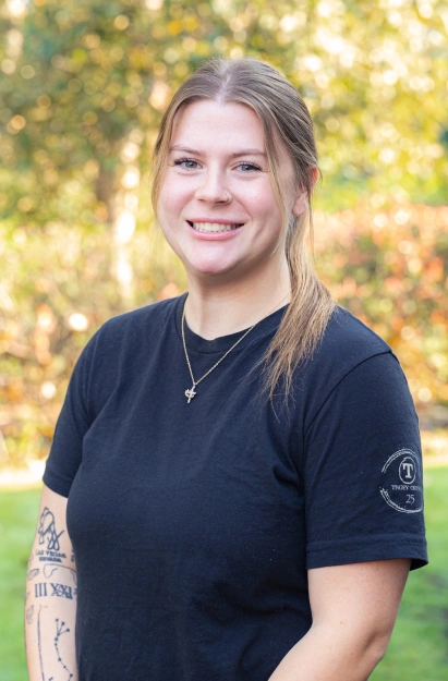 Woman in black shirt smiling outdoors with blurred green foliage background