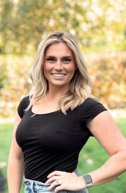 Professional woman smiling outdoors in black top with blurred green background.