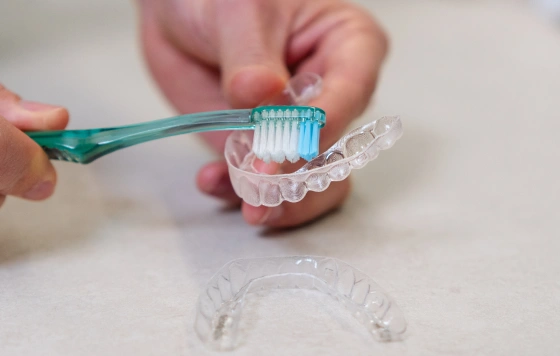 Person cleaning a clear aligner tray with a toothbrush